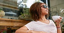 Portrait of attractive young african girl having a cup of coffee at cafe. Stylish young girl drinking coffee at sidewalk cafe - Stock Photo